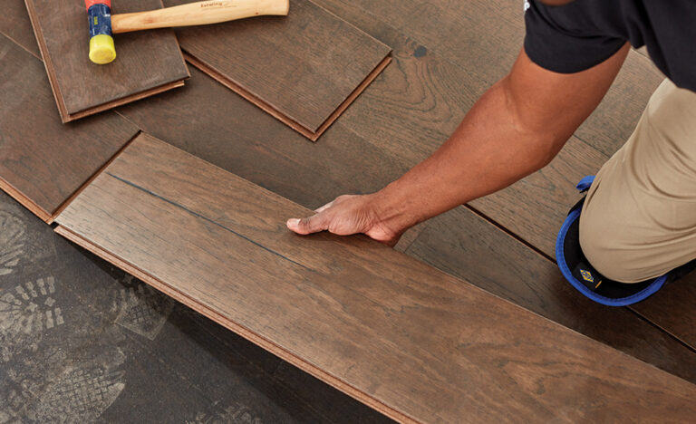 Installer fitting a dark hardwood plank into place with a hammer and tapping block